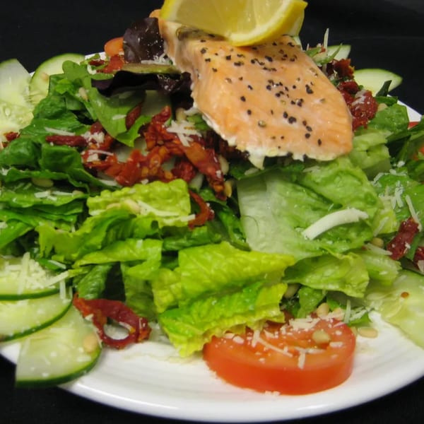 A fresh salad with grilled salmon, lemon, sun-dried tomatoes, cucumbers, and parmesan cheese.